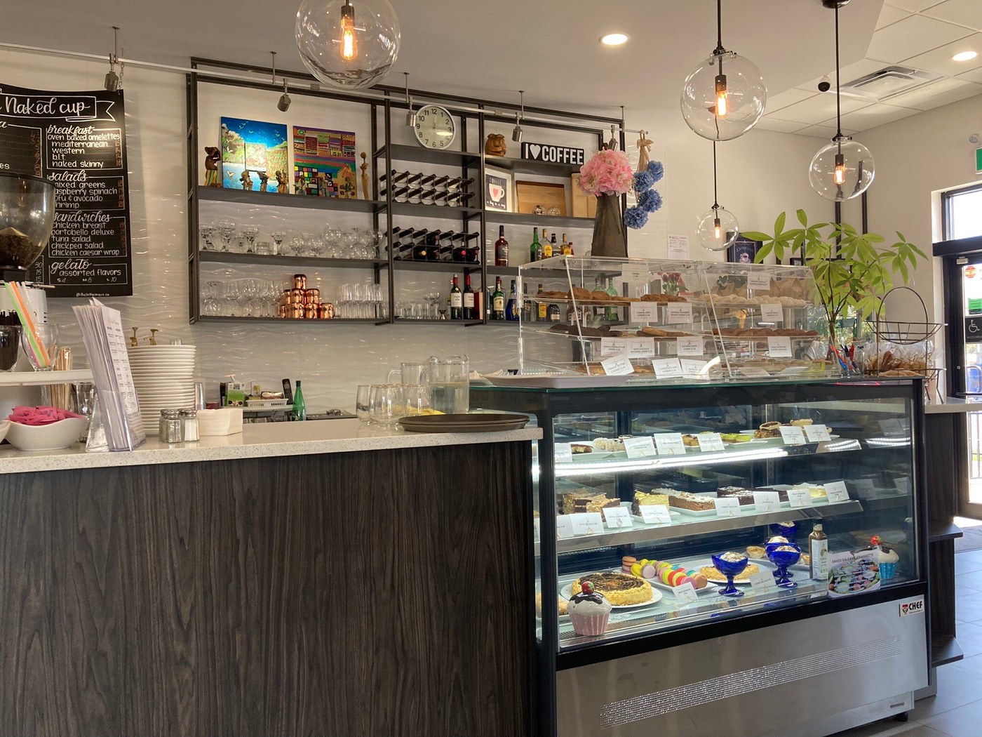 Café counter with a lit cake and macaron display, glassware shelves, flowers and globe pendant lights